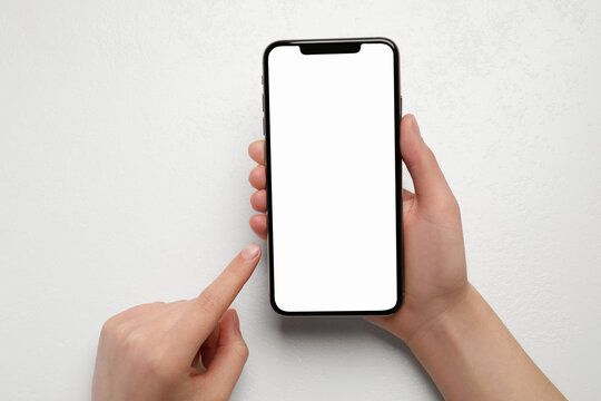 Woman Holding Smartphone With Blank Screen At White Table, Top View. Mockup For Design