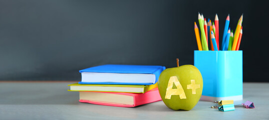 Apple with carved letter A and plus symbol as grade. School stationery on white table in classroom....