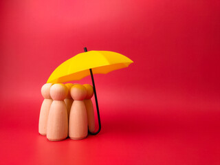 A group of wooden dolls are hiding under a yellow umbrella, protecting wooden peg dolls