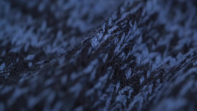 closeup rotation of knitted woolen crumpled dark blue fabric, detailed texture, macro. cozy wool blanket, bedspread, knitwear, warm sweater. dark blue knitted background.