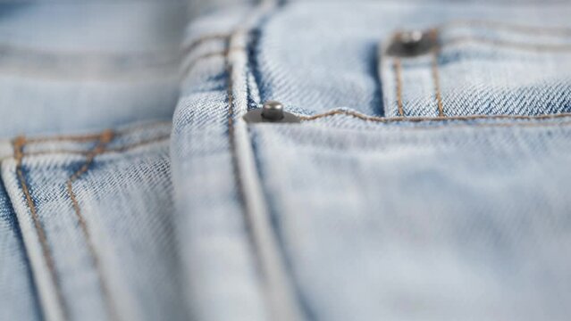 metal rivets on pockets of denim trousers and orange stitching on edges of the fabric. rotation of fabric of blue jeans in closeup details. abstract background, denim texture.