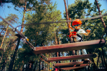 Child Wearing Protection Equipment Climbing Safely in Adventure Park. Kid walking in rope park...