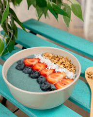 Smoothie Bowl with blue matcha or spirulina. Trendy breakfast. Healthy lifestyle. Strawberry, blueberry, granola, coconut. On turquoise table