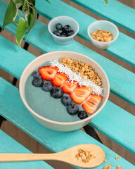 Smoothie Bowl with blue matcha or spirulina. Trendy breakfast. Healthy lifestyle. Strawberry, blueberry, granola, coconut. On turquoise table