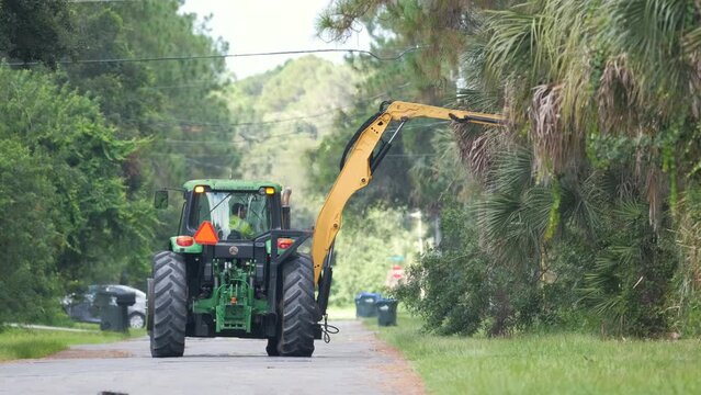 Public works utility tractor pruning trees and greenery braches on Florida rural street side