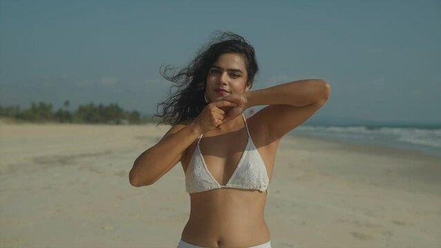 A beautiful Indian girl is applying sun protection cream on her arms and body on a beach