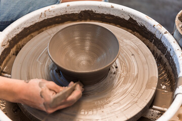 Woman working on a pottery wheel making a bowl with hand and tool using brown clay