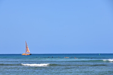 Surfers and sailors take advantage of a beautiful sunny day off the coast of Waikiki in Honolulu, Hawaii.