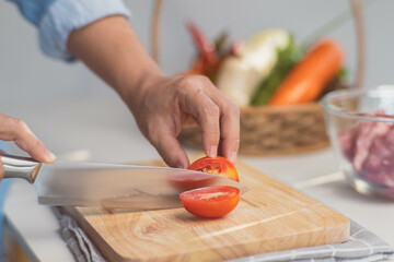 Cooking - Chef's hands are cutting tomatoes on the chopping board in the kitchen. Preparing pork stock with vegetables (broth) in a pot. Homemade bouillon recipe.