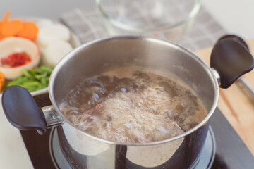 Homemade bouillon recipe. Chef's hands preparing pork rib stock (broth) with vegetables in the pot. Cook in the kitchen.