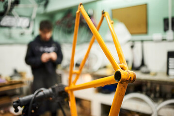 Orange bicycle frame held on a stand in a mechanical bike repair shop. Selective focus composition with copy space.