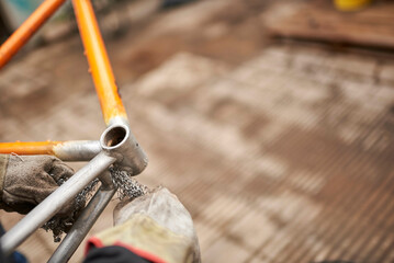 Manual work: unrecognizable worker using steel wool over a bicycle frame after passing a blowtorch over it to remove the paint, as part of the bike renovation process.