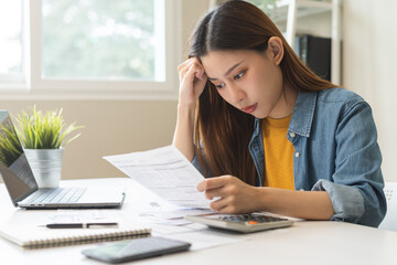 Stressed asian young employee, business woman calculate tax, income and expenses, hand holding bills of credit card for payment or payday on table at home office. Financial, finance people concept.