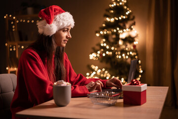 Obraz na płótnie Canvas Christmas online shopping. Female buyer with laptop. Woman buys presents, prepare to xmas eve, sitting at table with gift box. Winter holidays sales