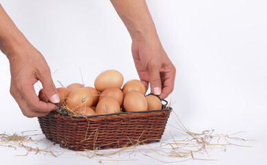 Fresh eggs in a beautifully placed basket with hands about to lift the basket on a white background
