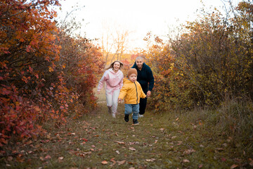 Fototapeta premium Beautiful young family on a walk in autumn forest. Parents running for little son. Happy family mother, father and child