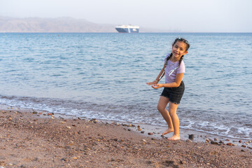 Cute little child playing on the beach, smiling and looking at camera. Little beautiful girl with braided hair.