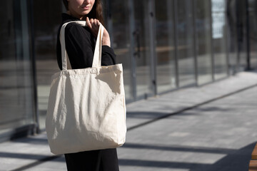 Woman holding white textile eco bag against urban city background. Ecology or environment...