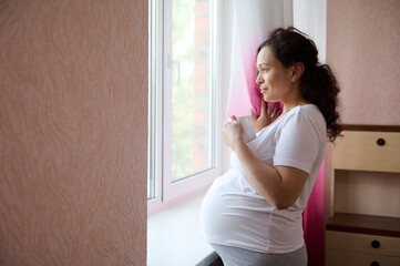 Beautiful pregnant woman future mother holds a cup of healthy tea, looking dreamily out the window...