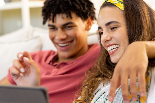 Smiling biracial young couple using digital tablet while relaxing on sofa in living room