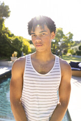 Portrait of biracial young man confidently standing at poolside against clear sky