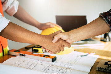 Successful deal, male architect shaking hands with client in construction site after confirm blueprint for renovate building.