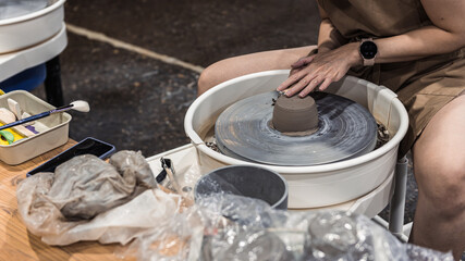 Woman working on a pottery wheel shaping and trimming a piece of dried pottery with a tool