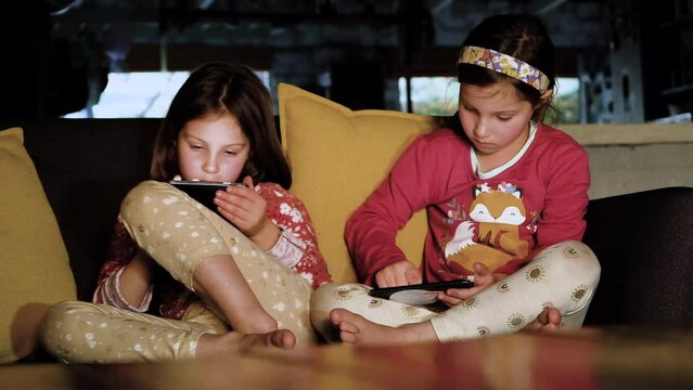 Screen time digital addiction as twin siblings girls are engrossed on their smartphones, no parental supervision