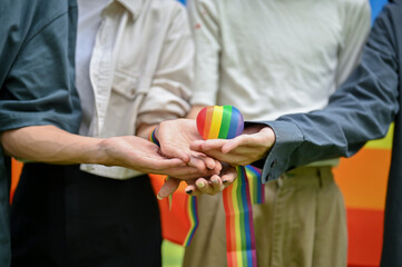 Diversity friends putting their hands together and holding the LGBT heart symbol.