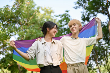 Happy and joyful young Asian girl holding the LGBT rainbow flag with her gay friend