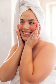 Closeup of plus size caucasian young woman wrapped with towels applying red eye patch in bathroom