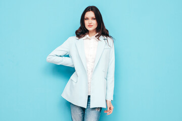 Portrait of young beautiful brunette woman wearing nice trendy blue suit jacket and jeans. Sexy fashion model posing in studio. Fashionable female isolated on blue. Cheerful and happy