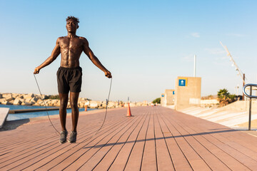 Fototapeta na wymiar African man jumping rope on a beach. Young athlete man training outside.