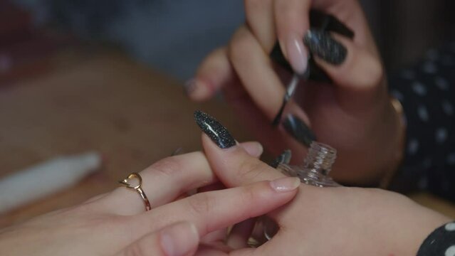 Manicurist applying clear base coat on a womans nail. Close up, gimbal