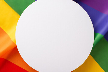 Top-down view of LGBT History Month arrangement with wavy rainbow flag, used as background, and an empty circle for text