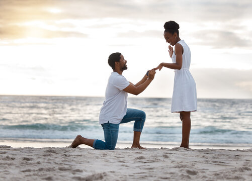 Love, beach and black couple with proposal, commitment and sunset with happiness, romance and holiday. Romantic, man or woman with engagement ring, asking and question with seaside vacation and smile
