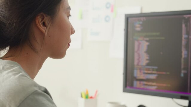 Close-up young Asia girl IT development programmer typing on keyboard coding programming fixing database code on computer monitor and laptop screen on table in workroom at house office.