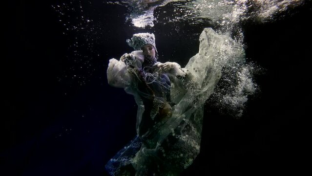 enigmatic woman in folklore gown and pearl crown swimming along underwater, fabulous female image