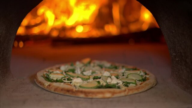 Slow motion close up of a veggie pizza cooked baked inside a traditional stone oven with wood burning into flames
