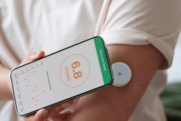 Woman synchronizing mobile phone with sensor on arm at home