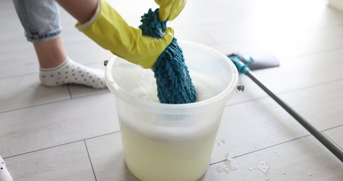Female hands in gloves squeeze a microfiber towel into bucket. Cleaning and filled with water and foam