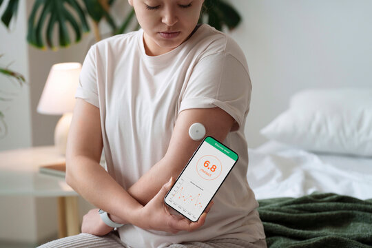 Woman with diabetes synchronizing smart phone with sensor on arm at home