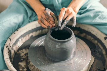 Messy hands of potter shaping pot at workshop