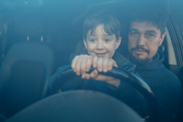 Smiling son learning to drive car with father seen through windshield