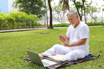 Naklejka na ściany i meble Asian senior man practice yoga exercise, stretching, tai chi tranining and meditation from computer on yoga mat for healthy in park outdoor after retirement. Happy elderly outdoor lifestyle concept
