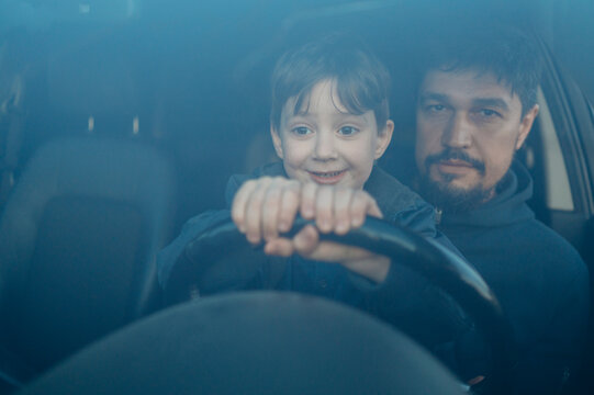 Smiling son learning to drive car with father seen through windshield - Powered by Adobe