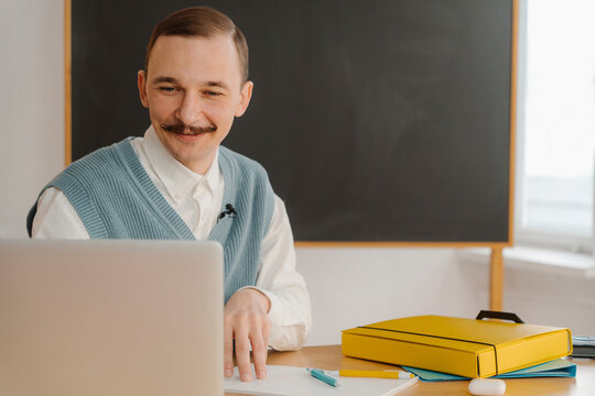 Smiling man sitting in classroom looking at laptop