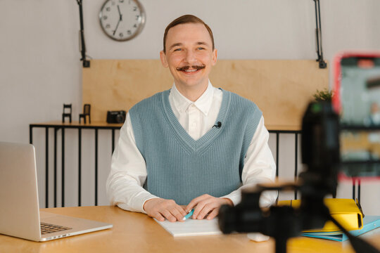 Smiling man sitting in classroom looking at camera recording online class