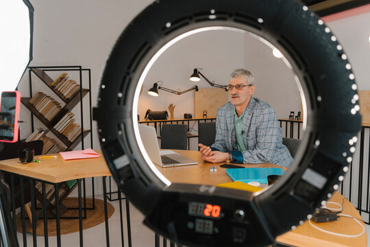Businessman recording online class in studio seen through ringlight