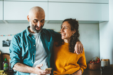 Man using smart phone by smiling woman in kitchen at home